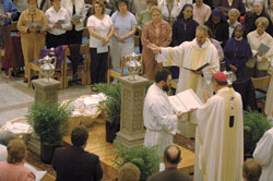 While members of the congregation look on, Deacon Thomas Kovatch, a member of St. Andrew Parish in Richmond, presents Archbishop Daniel M. Buechlein with one of the three oils blessed during the annual chrism Mass, celebrated on April 3 at SS. Peter and Paul Cathedral in Indianapolis. Seminarian Aaron Jenkins, a member of St. Mary Parish in Rushville, assists the archbishop.