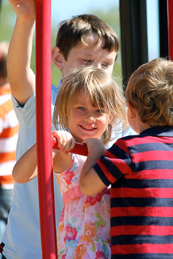 Surrounded by her brothers, Grace McVey flashes a smile as she plays on the new playground equipment that was recently dedicated at St. Charles Borromeo Parish in Bloomington in honor of the late pastor, Father Charles Chesebrough. Justin Dyer stands behind Grace while Liam McVey faces his sister. The three children of Robert and Marie McVey attend St. Charles Borromeo School. (Submitted photo)