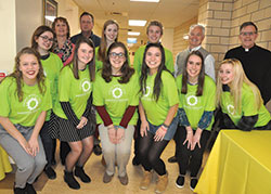 Recipients of scholarships for 2018 from the Brooke Nicole Lahr Memorial Fund for International Mission Work pose on March 4 in the Archbishop Edward T. O’Meara Catholic Center in Indianapolis. They are, from left, front row, Regan Happe, Dakota Dorsett, Elizabeth Poynton, Isabelle de Castro, Colleen Scheer and Ella Johnson. Back row, Katelynn Hexamer, left, Sally Jones, fourth from left, and Nicholas O’Connor, third from right. Also pictured, in the back row, Colleen Lahr, second from left, Brook Lahr’s mother, Mike Sexton, third from left, Brook’s uncle, Mark Lahr, second from right, Brook’s father, and Father Michael O’Mara, pastor of St. Gabriel the Archangel Parish in Indianapolis. (Photo by Sean Gallagher)