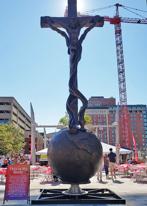 A 22-foot sculpture of Christ on a cross atop the world with blood from his wounds streaming into a chalice and a bowl filled with the Eucharist stands outside St. John the Evangelist Church across from the Indiana Convention Center in Indianapolis. The piece was created by Catholic sculptor Timothy Schmalz for the National Eucharistic Congress on July 17-21. (Photo by Natalie Hoefer)